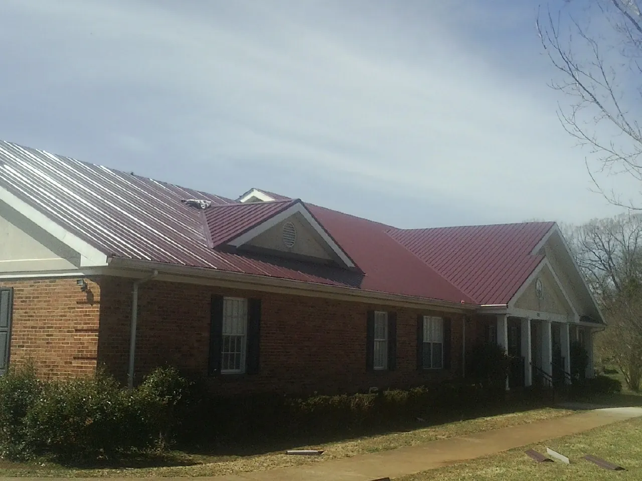Red metal roof with gabled entries on a long brick building, from a Hail Damage Roof Repair job in Willmar