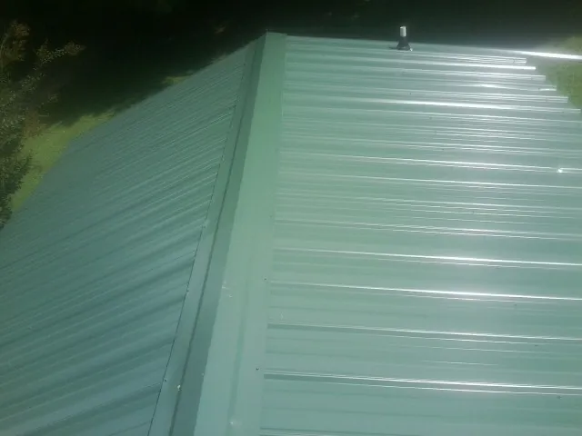 New green metal panels meeting at the ridge of a roof — Flat Roof Repair work by our crew in Willmar
