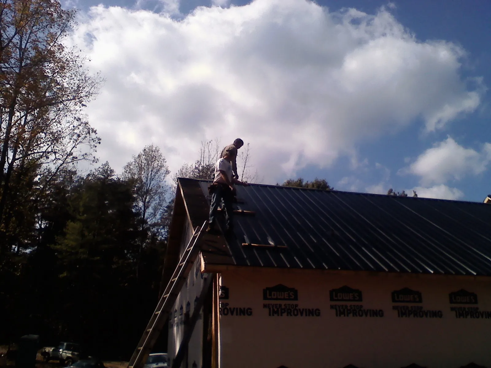 Roofer fastening dark metal panels high against a cloudy sky, from a Roof Inspection job in Willmar