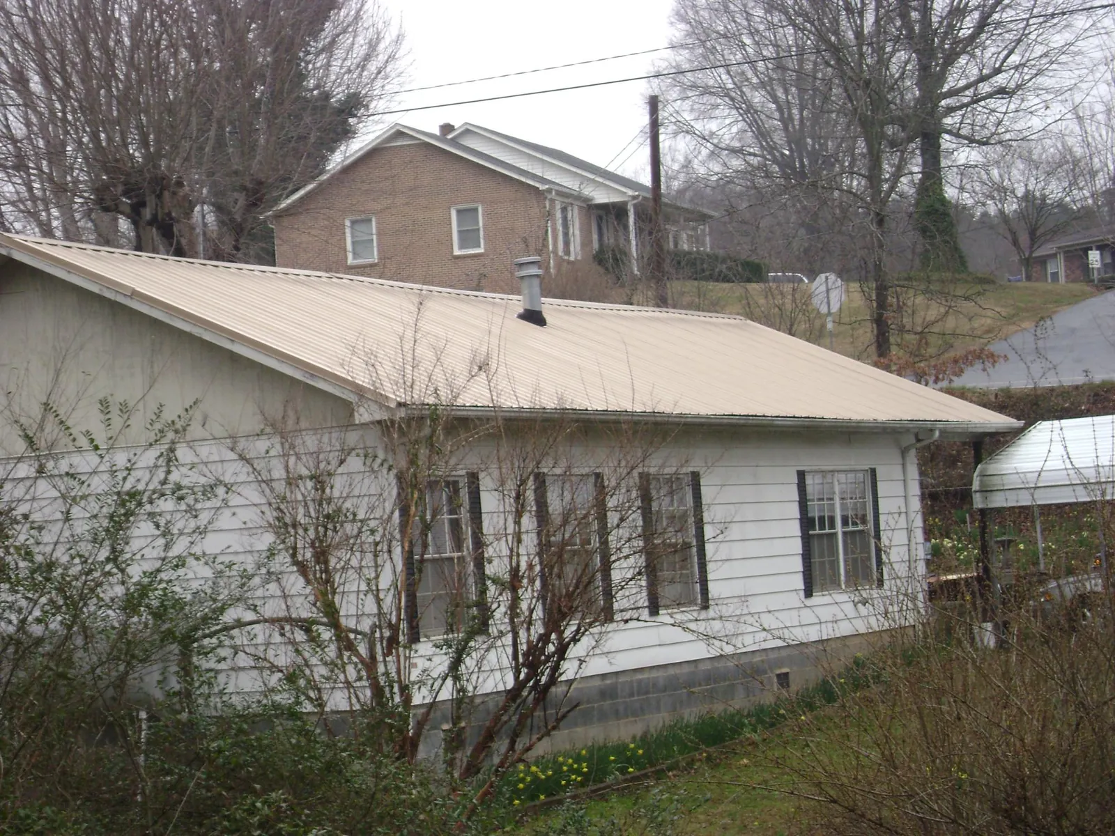Tan metal roof on a white sided house set into a hillside — Commercial Roofing by Roofing Brothers in Willmar