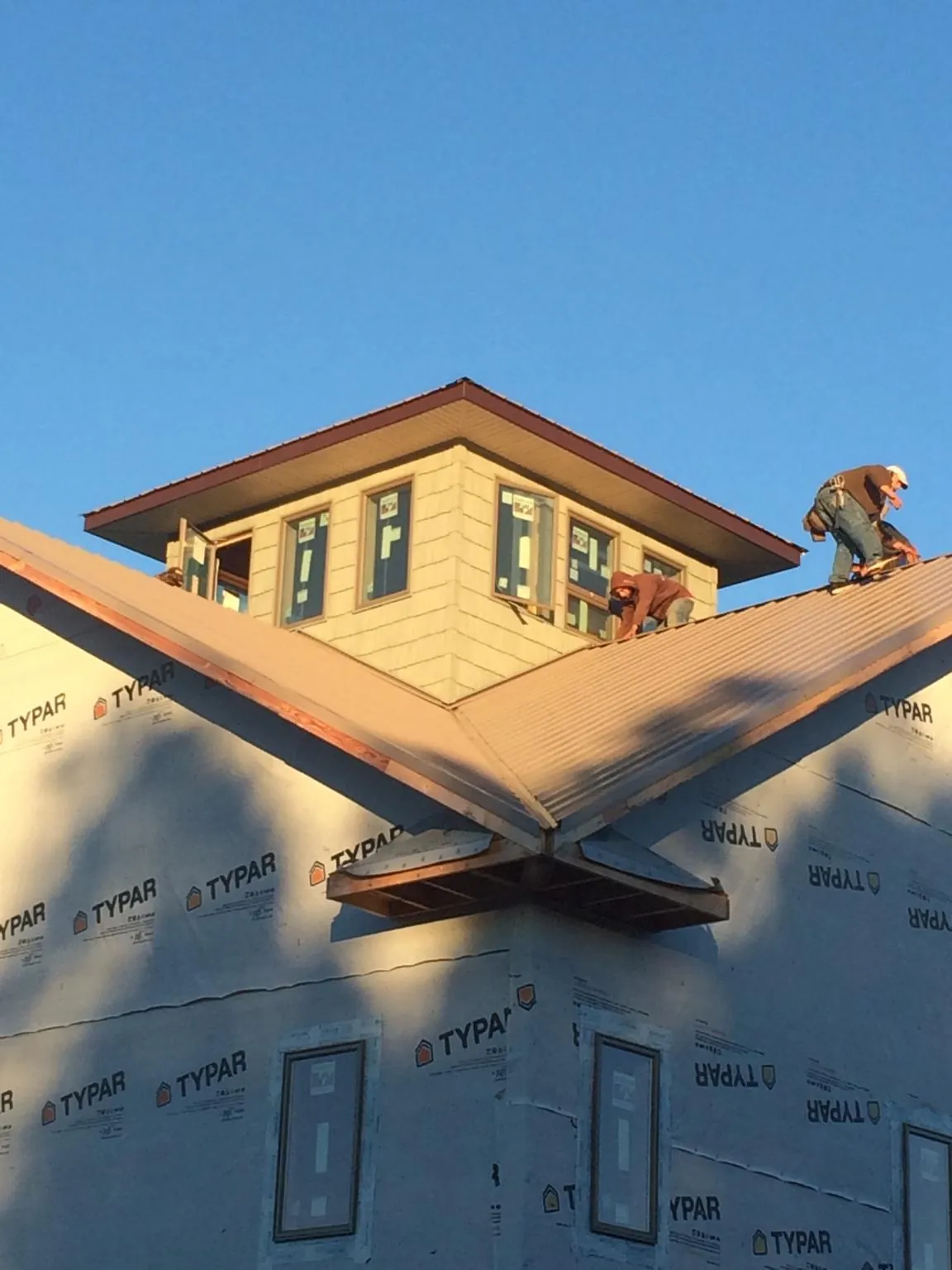 Roofers working around a rooftop cupola on a new metal roof at sunset — Roof Waterproofing in Willmar by Roofing Brothers
